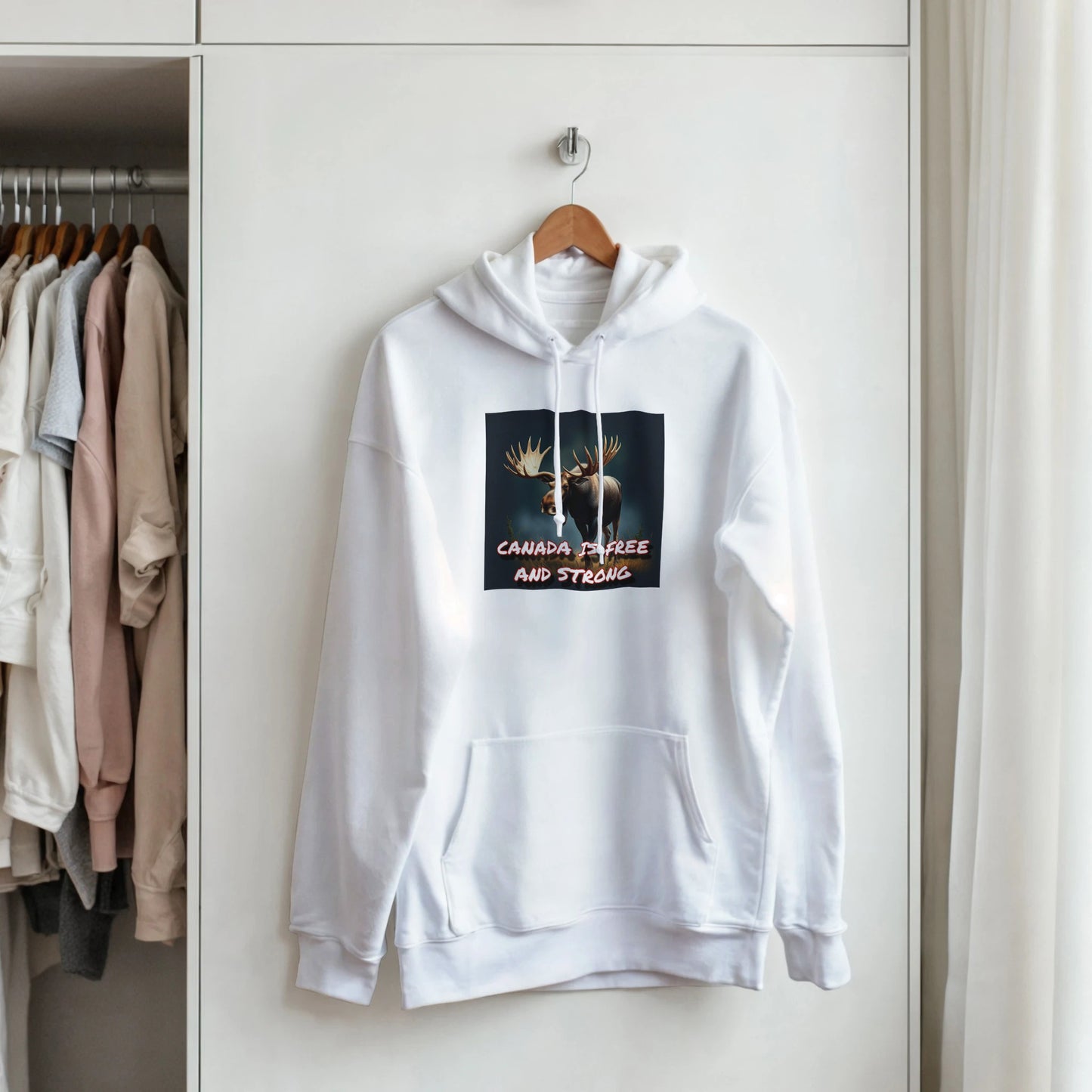 An Image of a pullover hoodie hanging on a hanger that says canada is free and strong with a picture of a moose on it